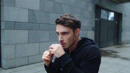 Focused Man Training Boxing Punch on City Street. Portrait of Young Man