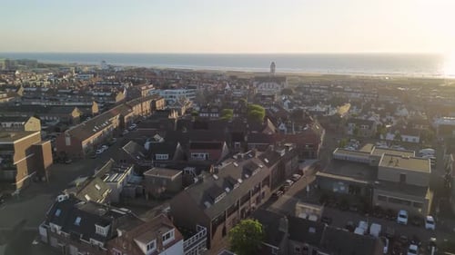 Aerial view of a coastal town at sunset with a white church, red-roofed houses, grassy dunes