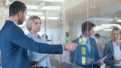 Businessman and Businesswoman Look at Sticky Paper On the Glass of the Office, Discussing Working P