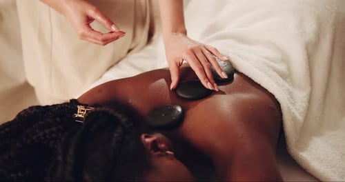 Back, hands and hot stone massage with customer in spa, on bed or table for natural wellness