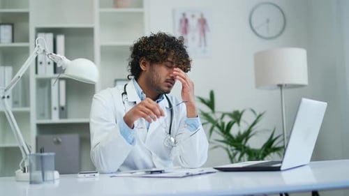 Tired doctor at workplace in office of the clinic work at computer Exhausted with a headache tension
