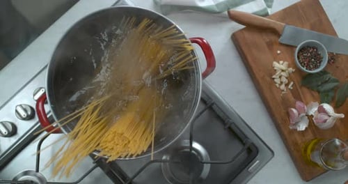 Spaghetti kocht leicht auf einem Gasherd neben frischem Knoblauch in sanftem Licht