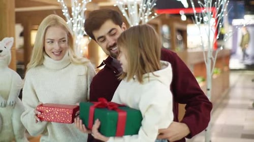 Cheerful Young Parents Give Gifts to Daughter in Shopping Mall Spending Weekend Together Standing on