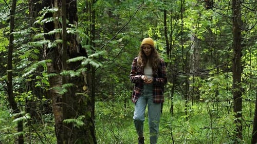 Young Biologist in Casual Attire Strolls Through a Vibrant Green Forest Examining a Specimen While