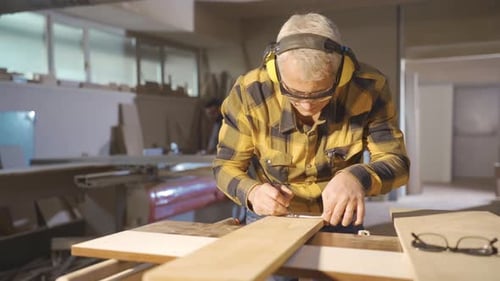 Gray Haired Woodworker Marking Wood with Pencil