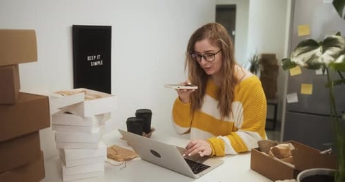 Young Woman Talks on Phone While Using Laptop