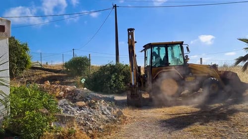 close up of an excavator cleaning the ground next to a house on a sunny day with a blue sky