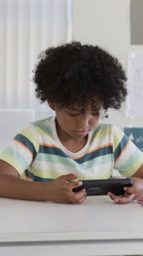 Vertical video: Looking down, kid tapping device at table, adjusting grip to focus, pastel tee
