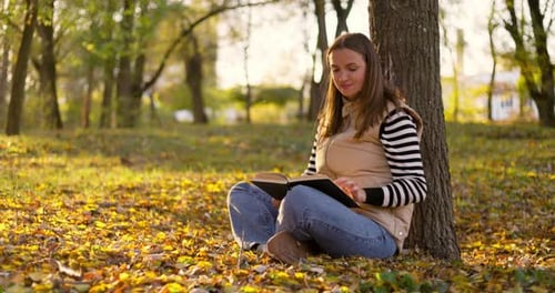 Woman Reading a Book While Sitting Under a Tree in an Autumn Park