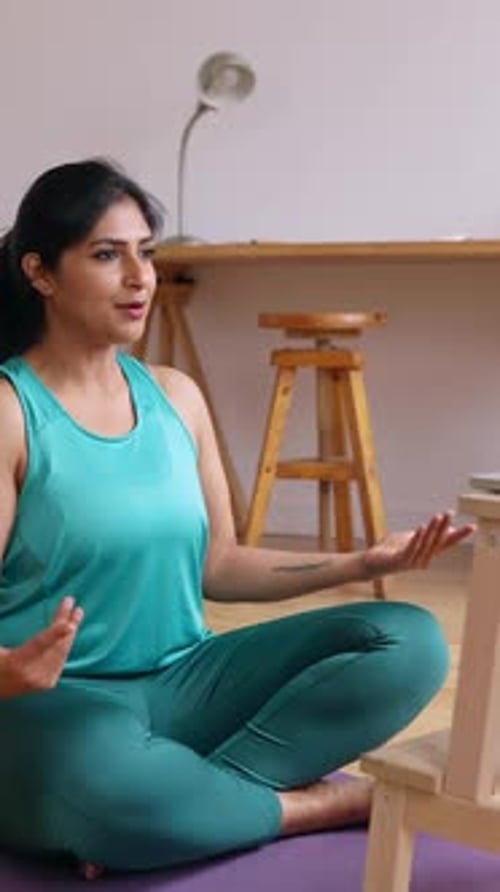 Indische Yoga-Trainerin sitzt auf einer Matte und macht Online-Meditationskurs zu Hause