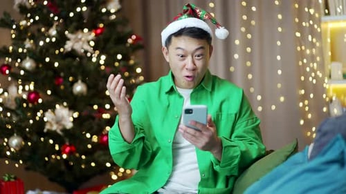 Excited Man Celebrates with Phone by Christmas Tree