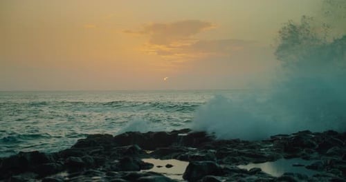 Ocean waves spalsh at sunset with soft evening orange light on sea water. Clouds on sky. Rocky volca