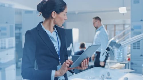 Stylische Ingenieurin für Industrierobotik verwendet Tablet-Computer, um Roboter-Ar zu programmieren und zu manipulieren