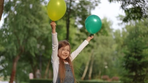 A Cheerful Girl Holding Colorful Balloons in a Lush Green Park Setting Filled with Joy