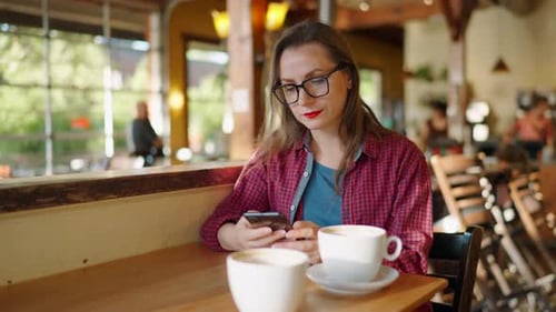 Woman is Using Smartphone and Drinking Coffee in the Cafe