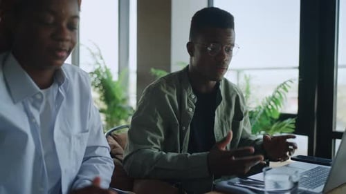Black Male and Female Coworkers Analyzing Data on Digital Devices in Cosy Cafe