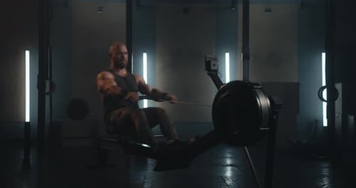 Athletic Bearded Man in a Tank Top Exercising on a Rowing Machine in a Contemporary Gym