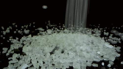 Camera dolly forward - Coarse salt falling on a black mirrored surface