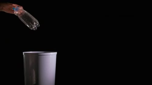 Hand Throws Plastic Bottle into Gray Trash Can