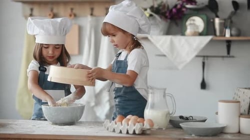 Two kids in white chef uniform putting cleared flour into the bowl on the kitchen