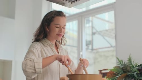 Young Woman Stirring Food in Kitchen with Wooden Spoons