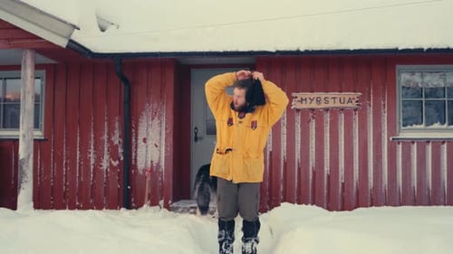 Man Puts on Beanie Outside Snowy Cabin