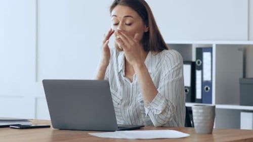 Müde Geschäftsfrau reibt sich bei der Arbeit am Laptop die Augen