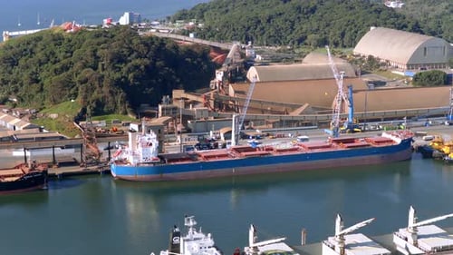 Slow aerial approach towards docked cargo ship at industrial port, Brazil.
