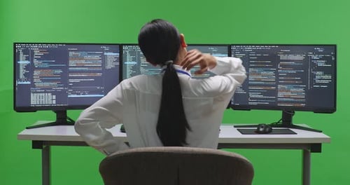 Tired Asian Woman Developer Stretching While Write Code With Multiple Screens In Green Screen Studio