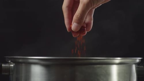 Hand Adding Red Spice to Steaming Pot