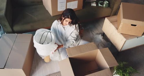 Young Woman Packs Lamp in Box at Home