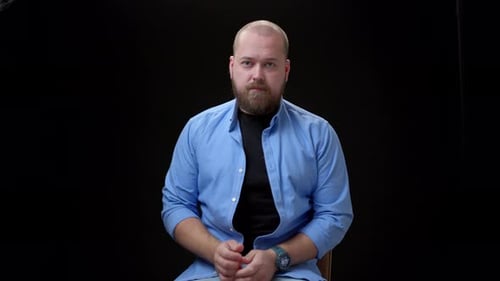 Bearded Man Sits and Talks on Black Background