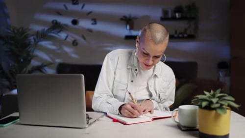 Woman Works at Laptop and Writes in Notebook