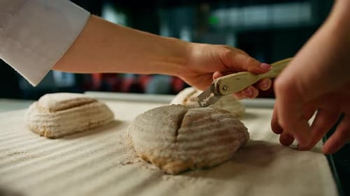 woman baker cuts patterns on raw bread rolls with a professional baker's knife before baking bakery