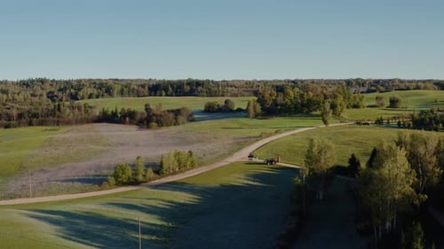 Aerial countryside landscape in a sunny morning with gravel road and tractor.