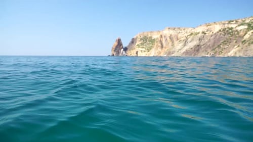 Sea Water Surface Camera Flies Over the Calm Azure Sea with Volcanic Rocky Shores on Background