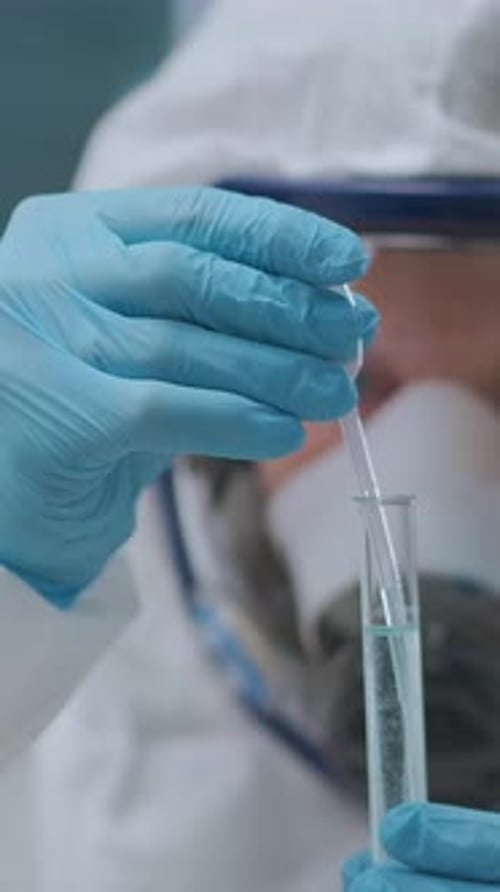 Wissenschaftler in Schutzausrüstung führen ein sorgfältiges chemisches Experiment mit Pipette und Reagenzglas durch