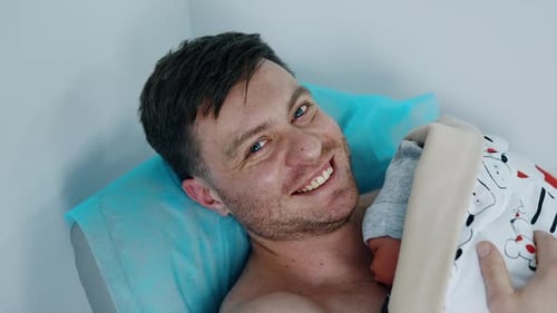 Happy Father Cradling Newborn Baby in Hospital