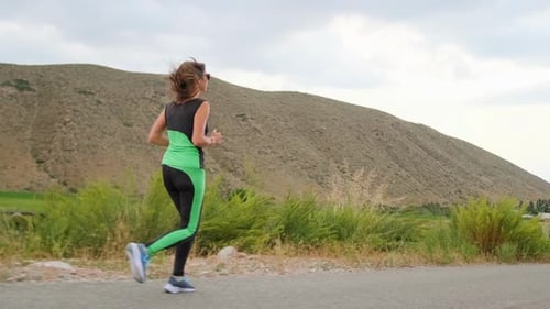 Young Woman Runs a Mountain Road on an Overcast Day Building Endurance