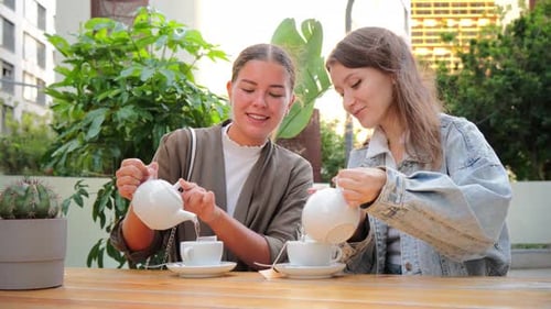 Two Young Women Pouring Tea at an Outdoor Cafe