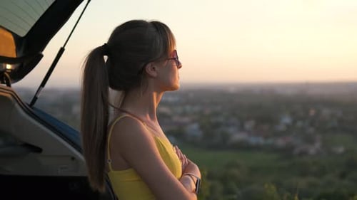 Happy Young Girl in Summer Dress Standing Near Her Car Enjoying Sunset View