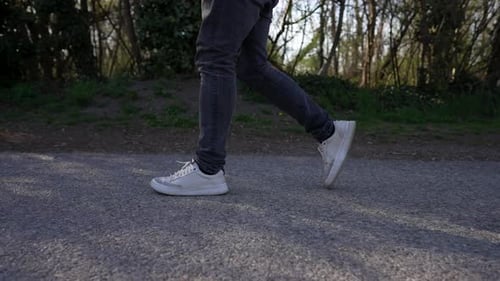Nahaufnahme von Menschenbeinen, die auf einer gepflasterten Straße mit Bäumen im Hintergrund laufen