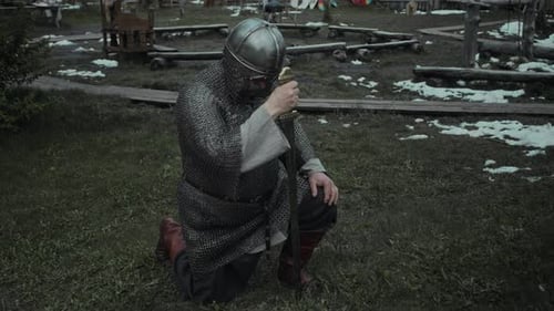Knight in Chainmail and Helmet Kneeling with Sword to Pray before Battle