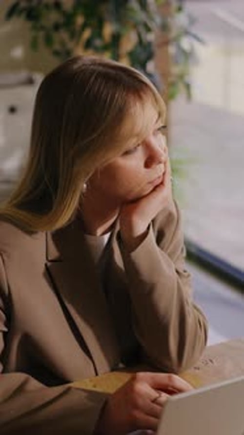 Focused Young Professional Woman Working on Laptop at Wooden Desk in Modern Office with Natural