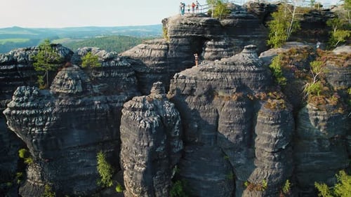 Aerial view of a rock climber scaling the side of a massive, weathered rock face amidst a lush green