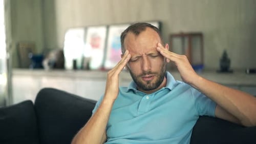 Man Massaging Temples Sitting on Couch in Living Room