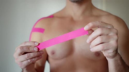 Adult Male Prepares Kinesiology Tape on Shoulder