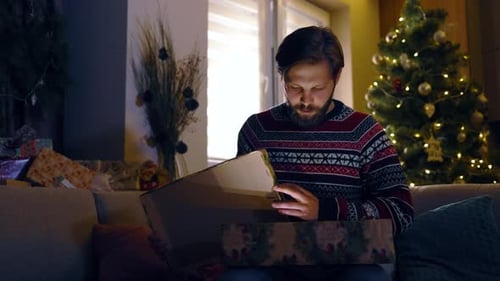 Man opens Christmas gift on couch at home