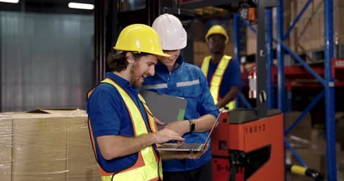 caucasian male warehouse manager and supervisor reviewing shipment records on laptop standing beside