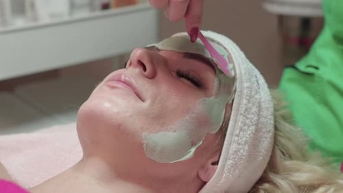 Beautician Applying Facial Mask For Peeling Treatment on Face of Woman in Spa Salon, Close Up